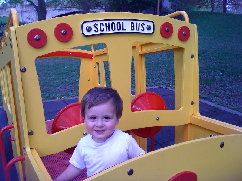 A young child is smiling while sitting in a play structure designed to look like a school bus.