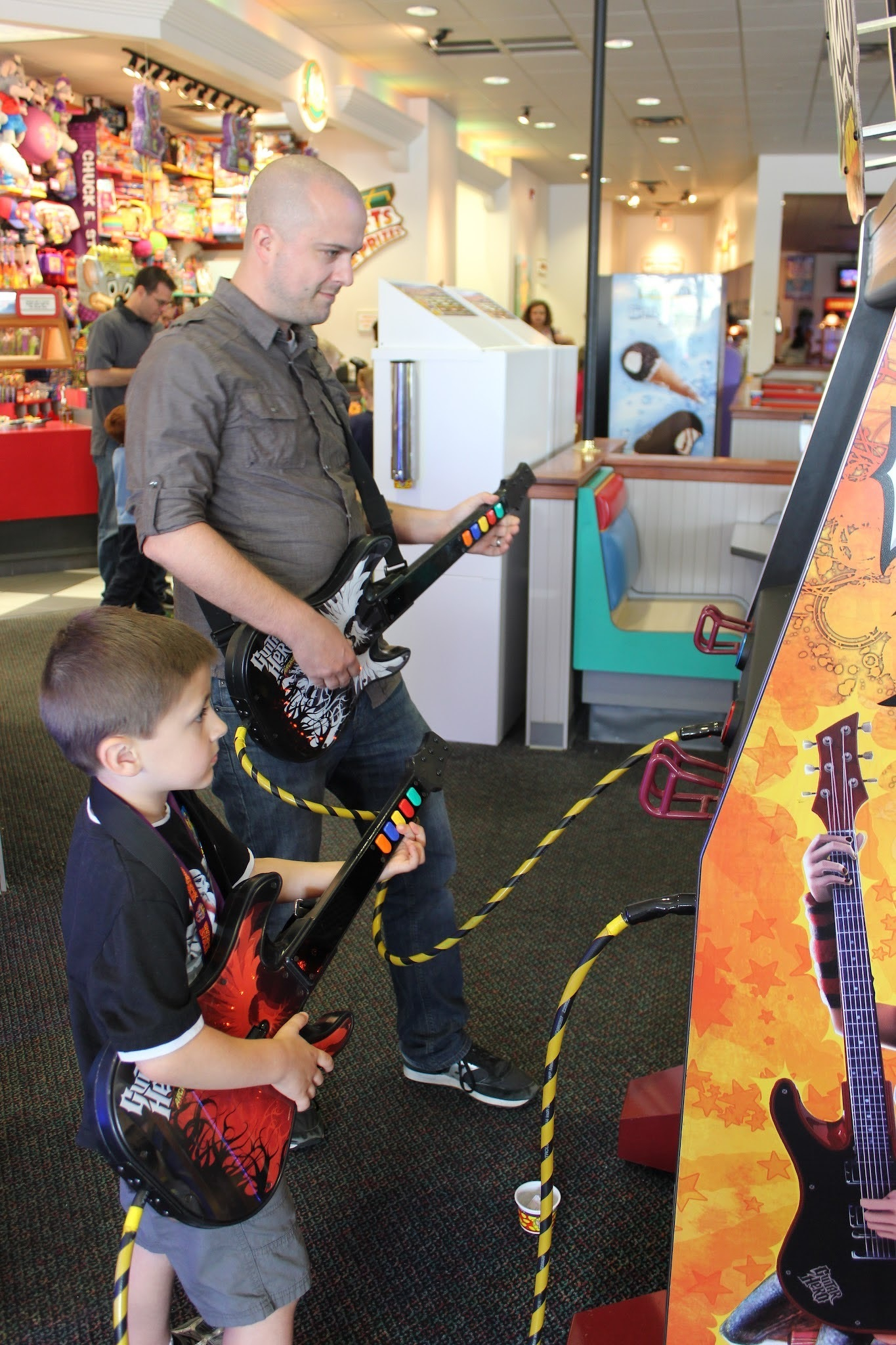 A man and a child are playing a guitar video game at an arcade.