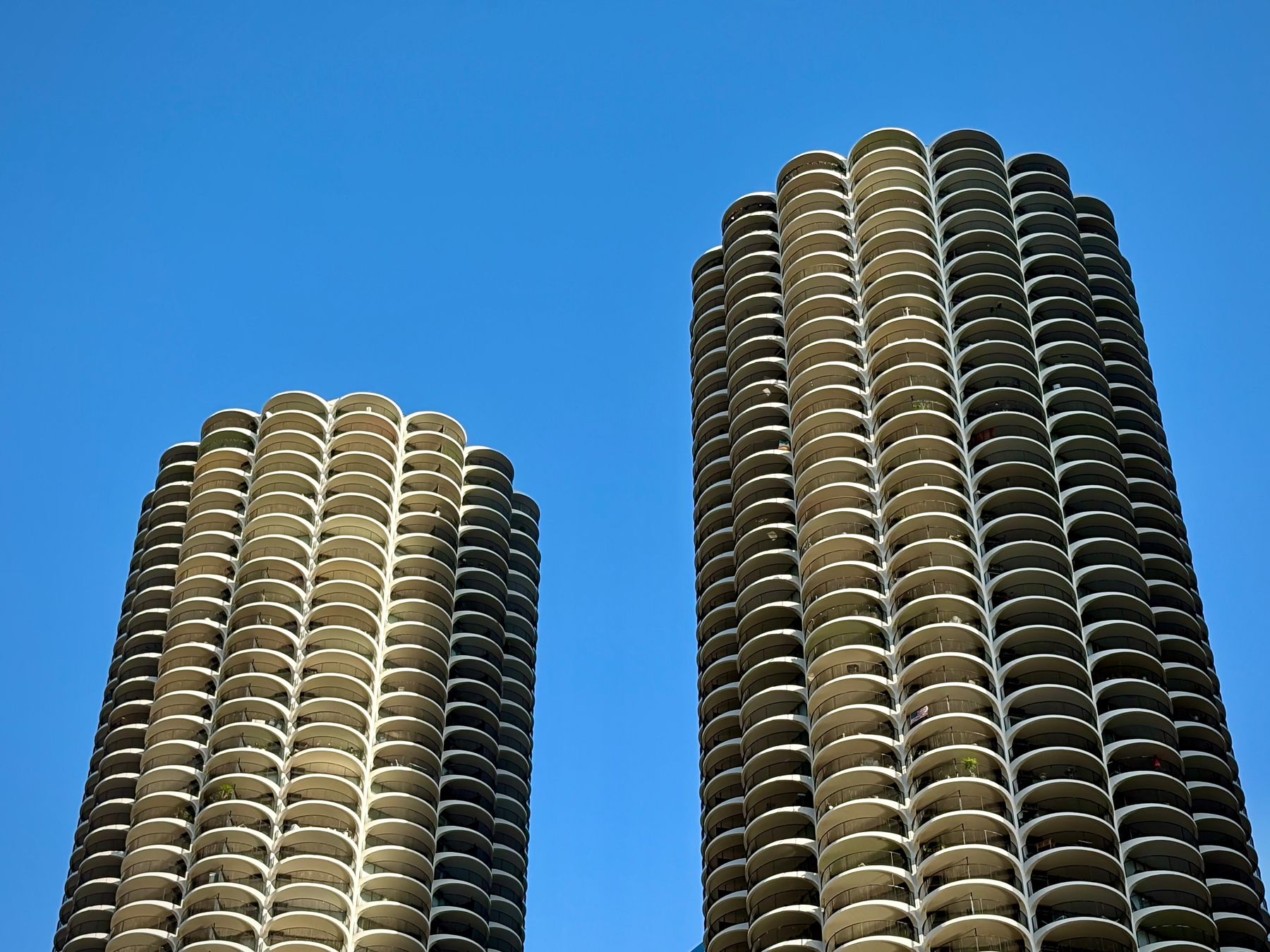 Two cylindrical skyscrapers featuring multiple round balconies rise against a clear blue sky.