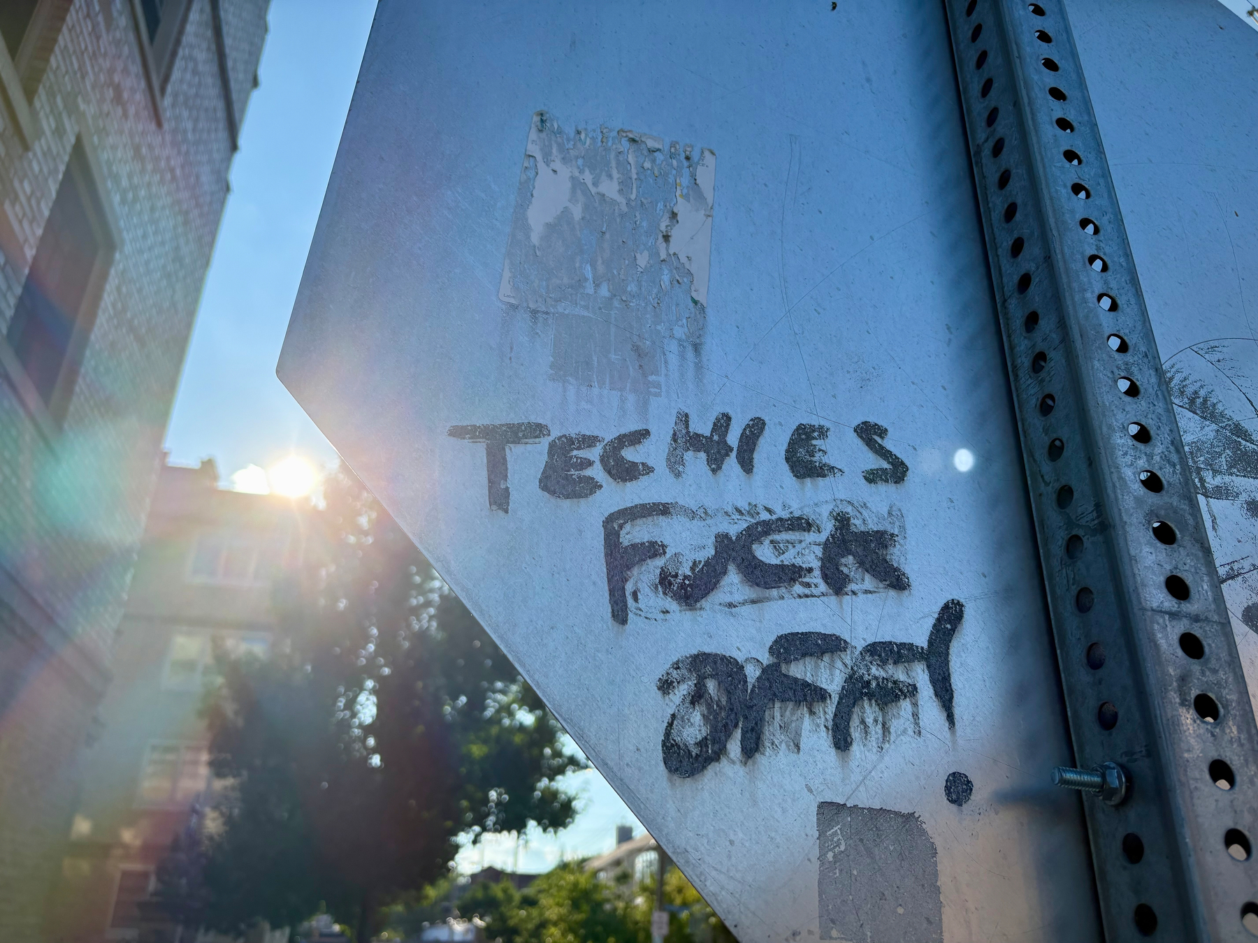 A street sign is spray-painted with the phrase TECHIES FUCK OFF! in black lettering.