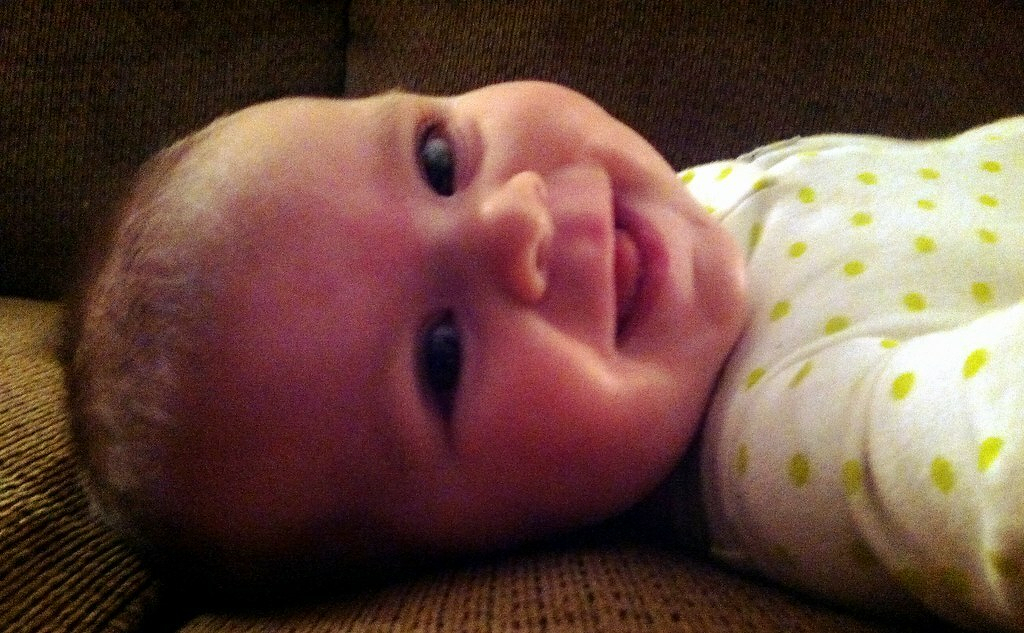 A baby wearing a polka dot outfit is lying down and smiling at the camera.