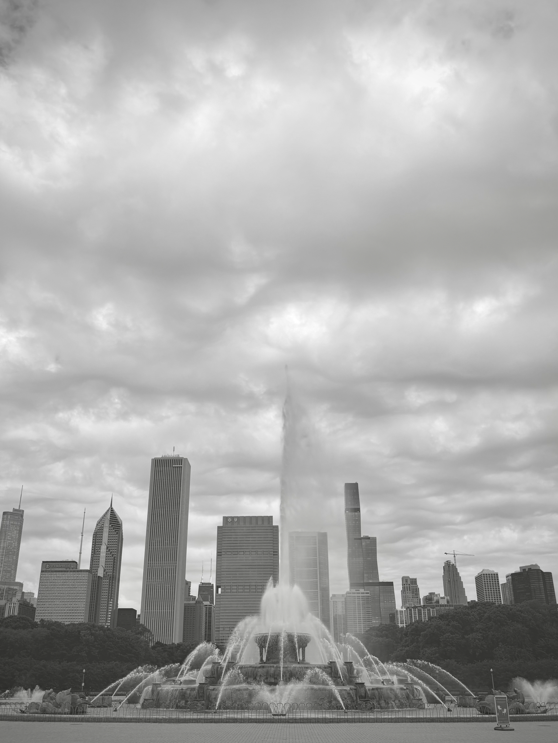 A city skyline features a prominent fountain in the foreground under a cloudy sky.
