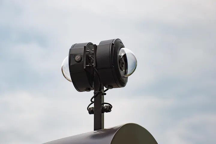Auto-generated description: A surveillance camera with dual lenses is mounted on a pole against a cloudy sky.