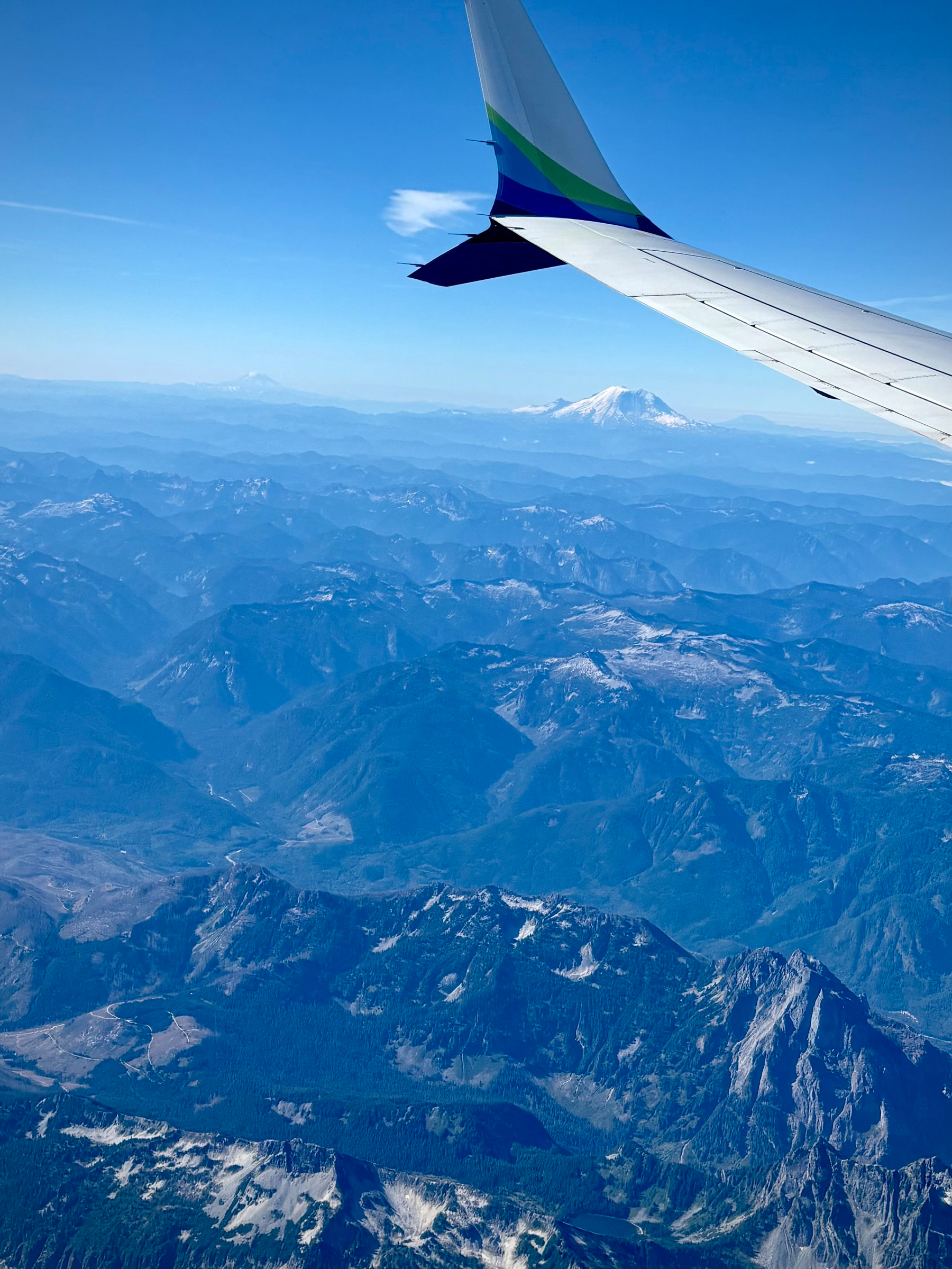 Aerial view of a mountain range with snow-capped peaks seen from an airplane window showing part of the wing.