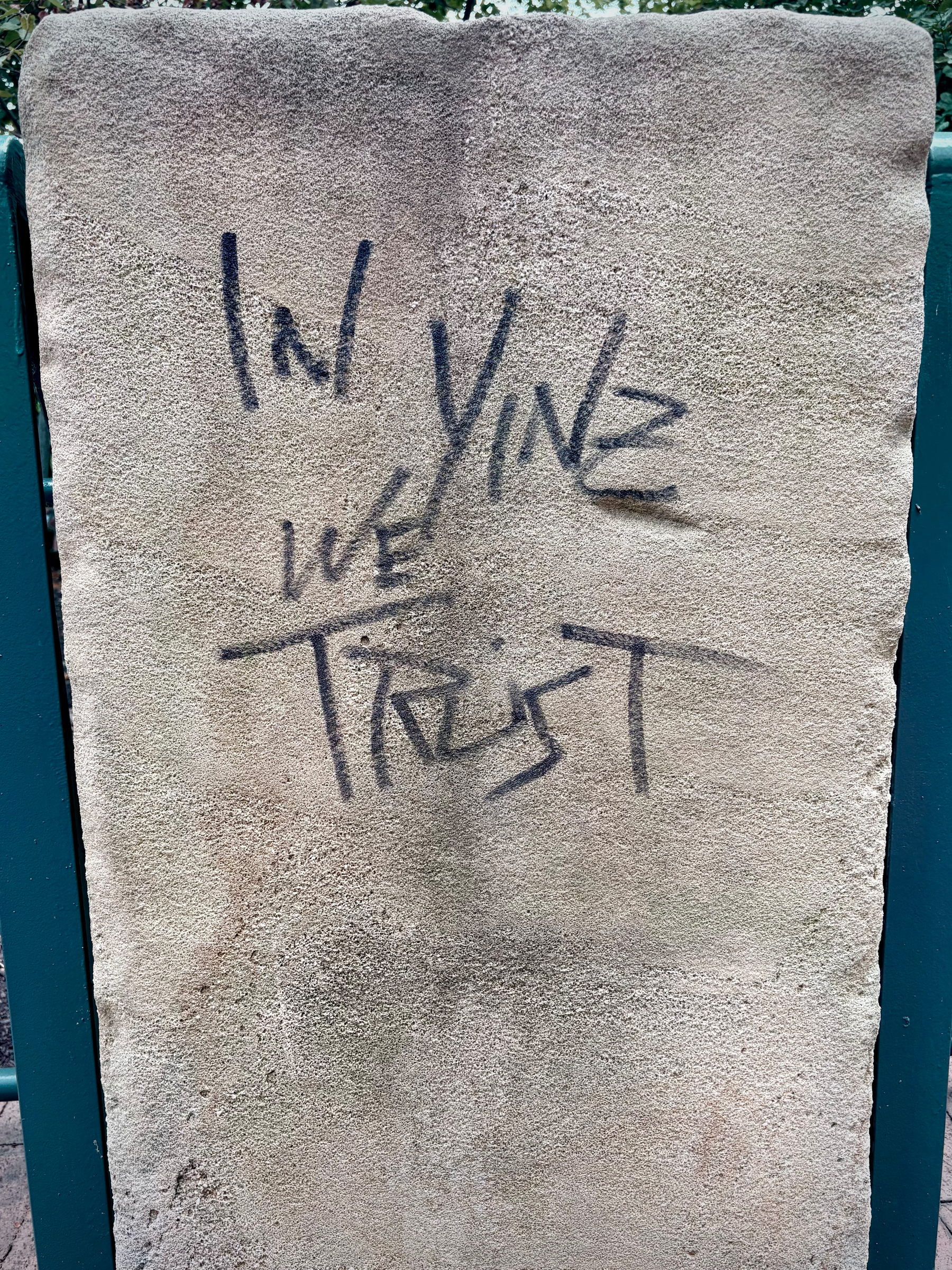 The words In Yinz we Trust are spray-painted in black on a rough, beige vertical surface.
