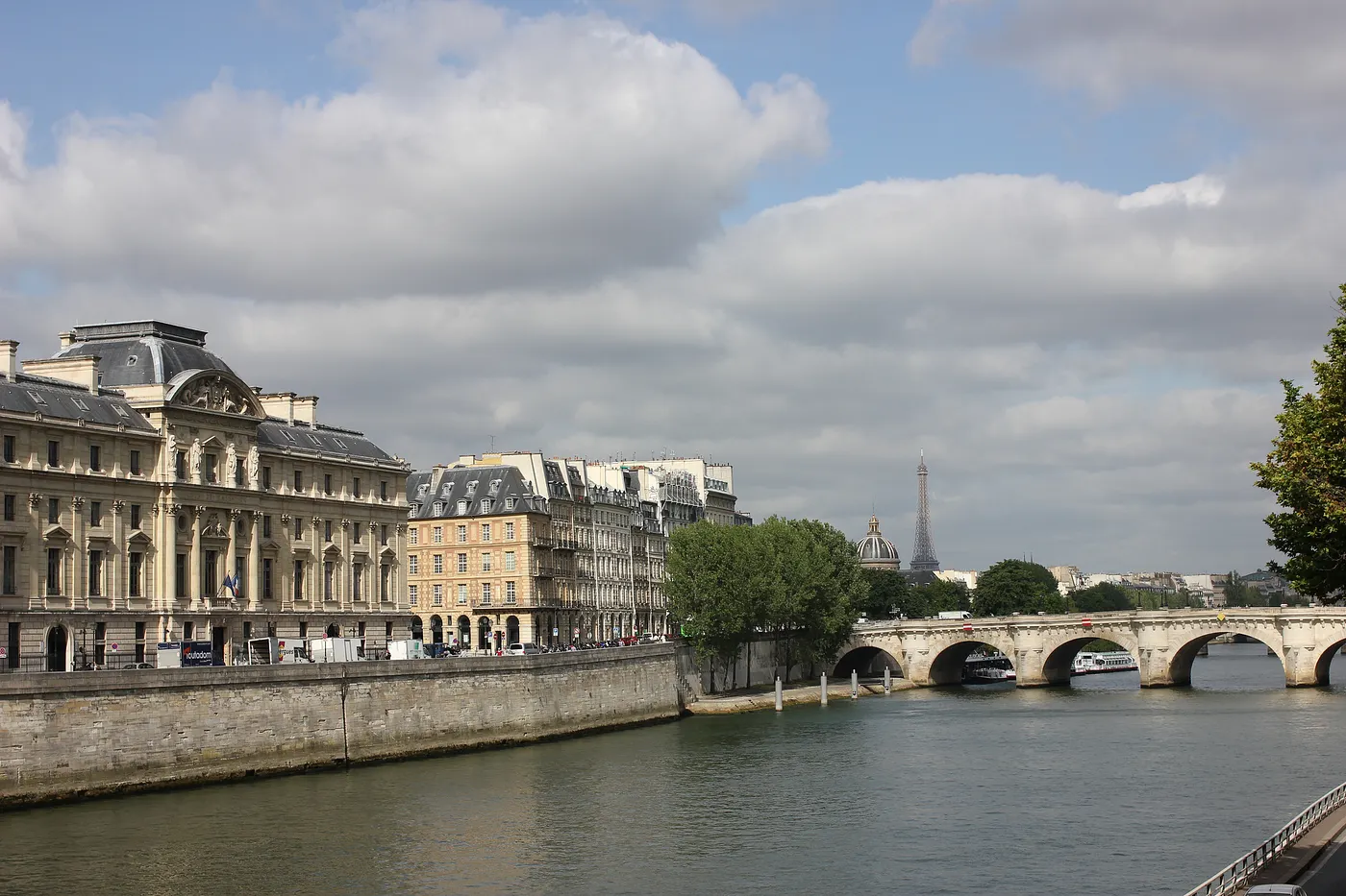 Auto-generated description: A scenic view of the Seine River in Paris, featuring historic buildings, a bridge, and the Eiffel Tower in the background.