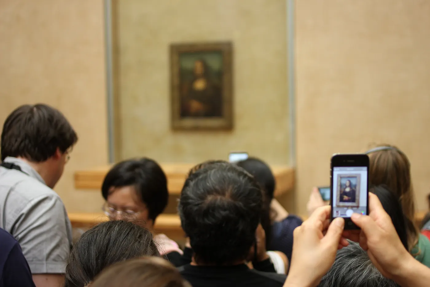 Auto-generated description: A group of people are gathered in front of the Mona Lisa while some take photos with their phones.