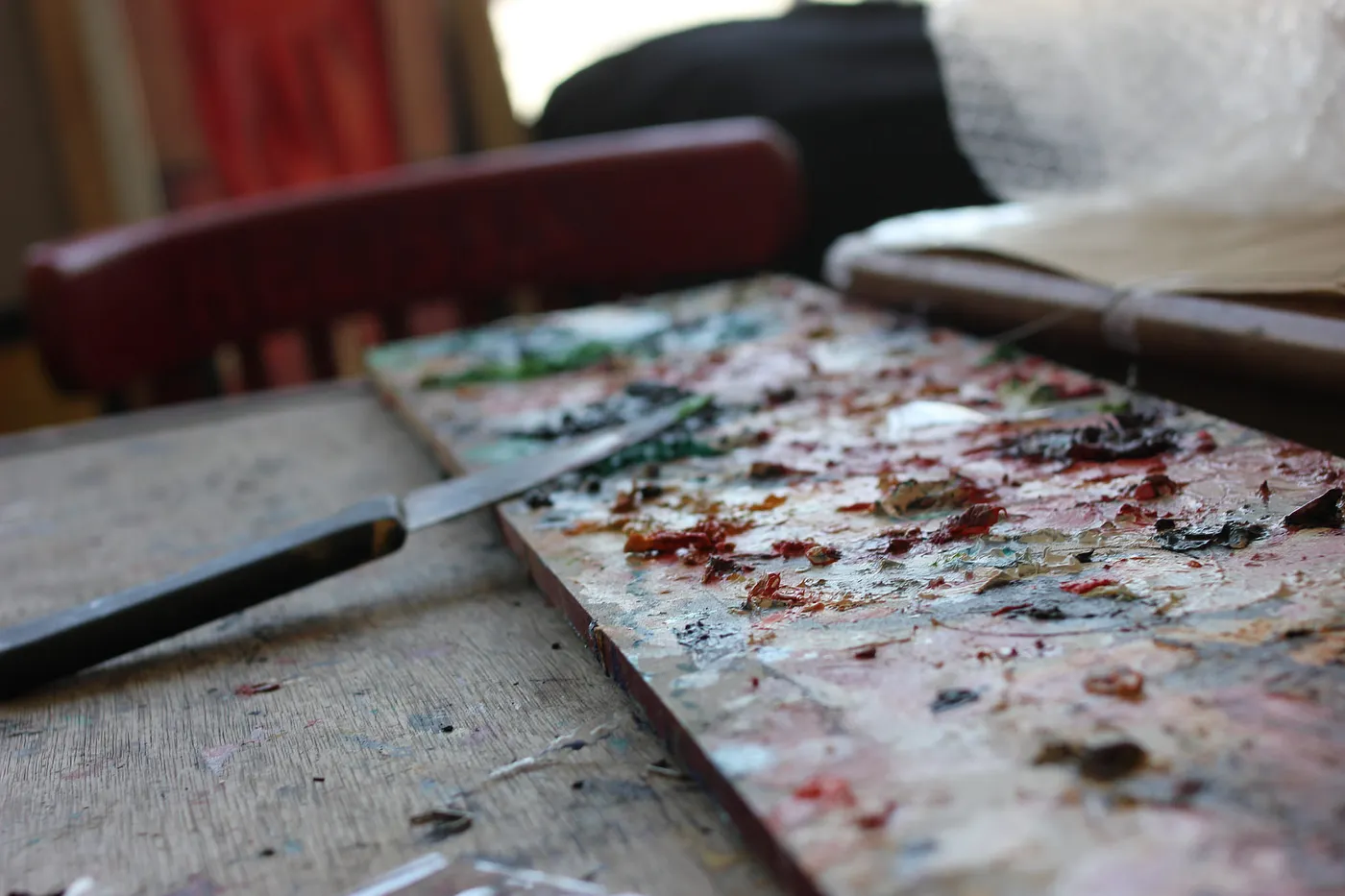 Auto-generated description: A painter's messy palette is accompanied by a knife on a wooden table.