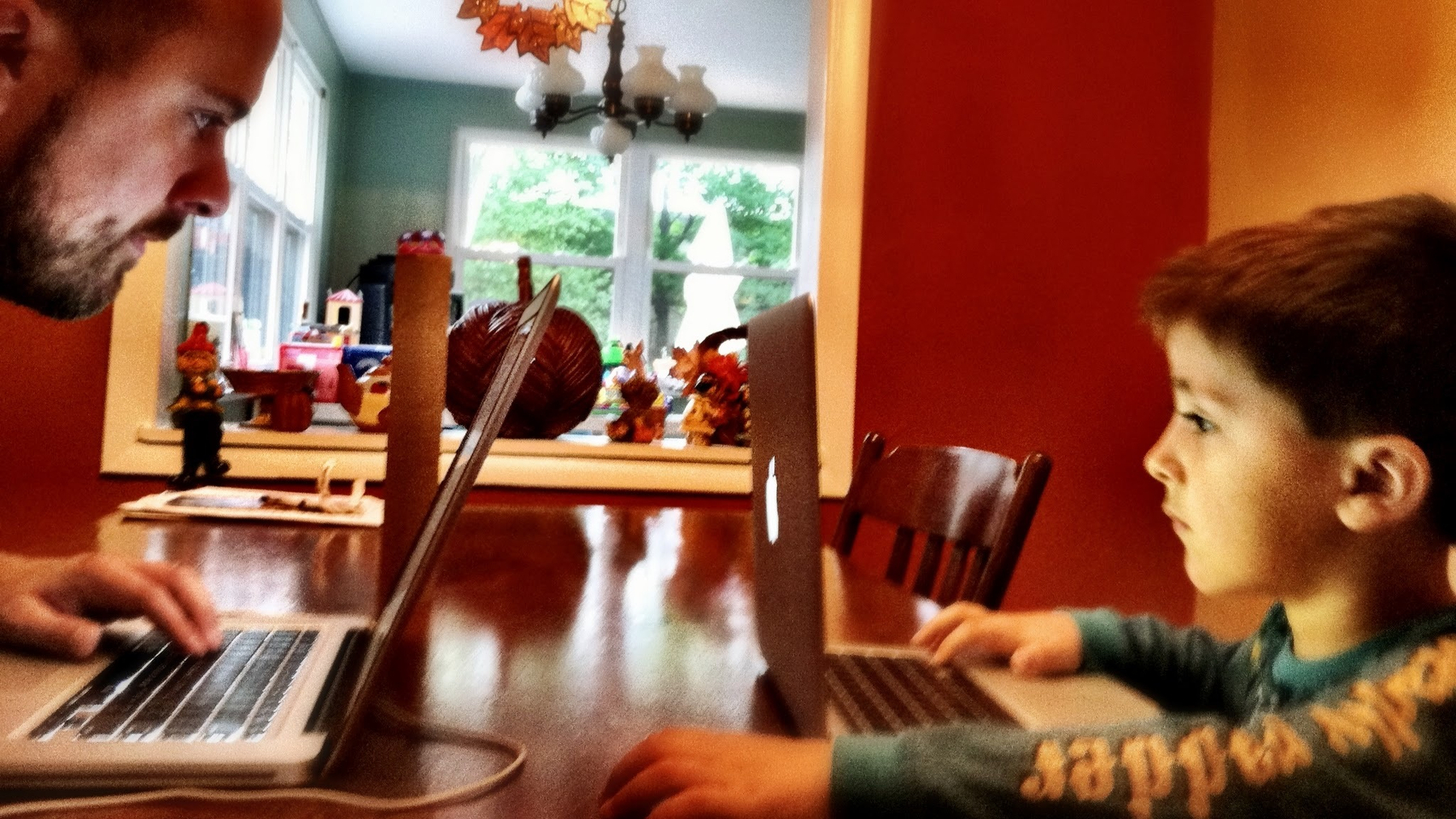 An adult and a child are sitting at a table using laptops facing each other.