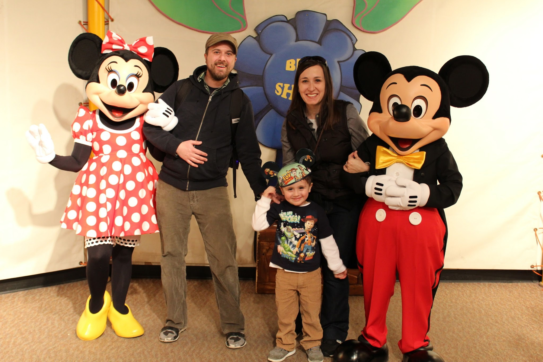 A family poses for a photo with two people dressed as Minnie and Mickey Mouse in front of a colorful backdrop.