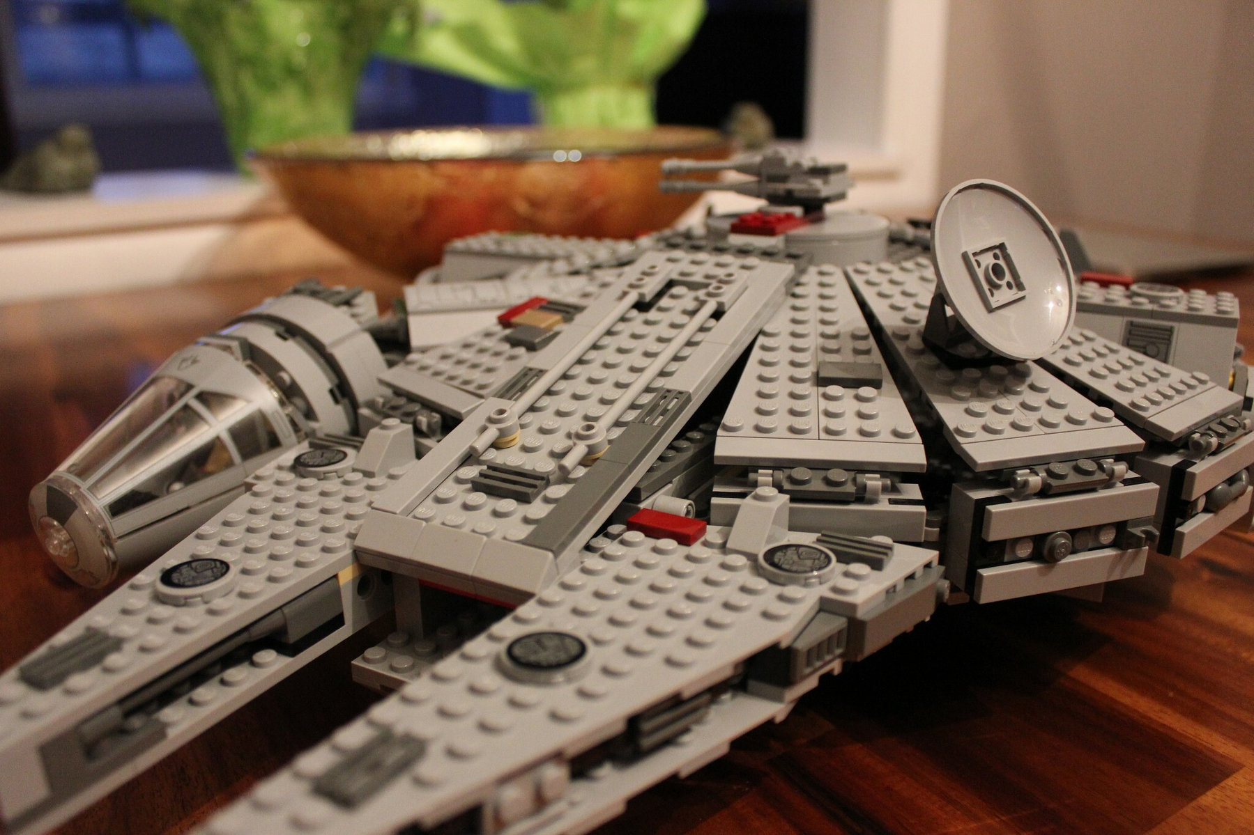 A detailed LEGO model resembling a spaceship is displayed on a wooden surface with decorative items in the background.