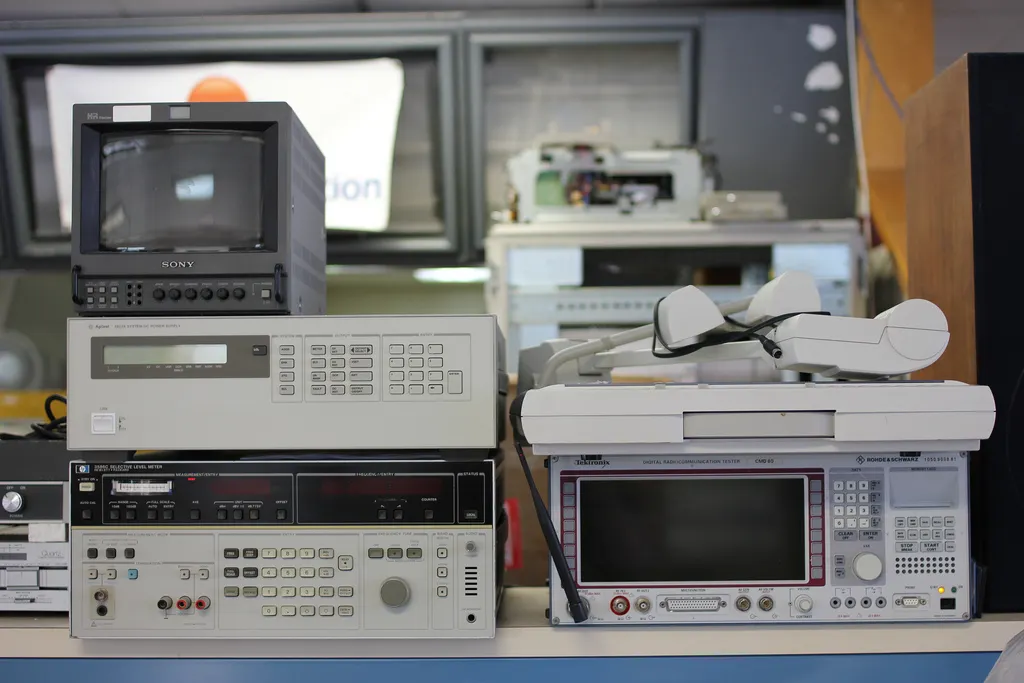 Auto-generated description: Various pieces of electronic testing equipment and monitors are stacked on a table.