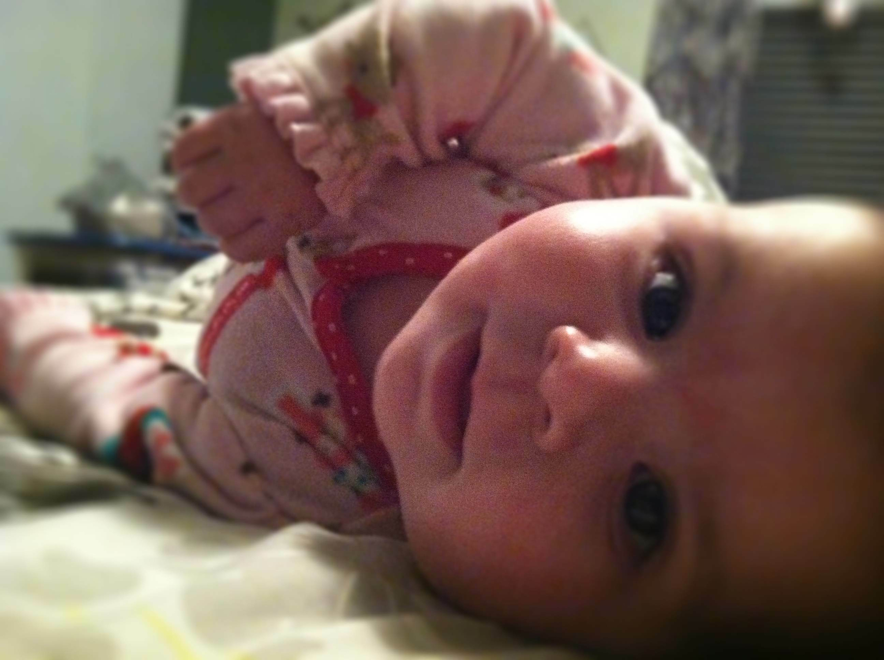 A baby in pajamas is lying on their side with a subtle smile.