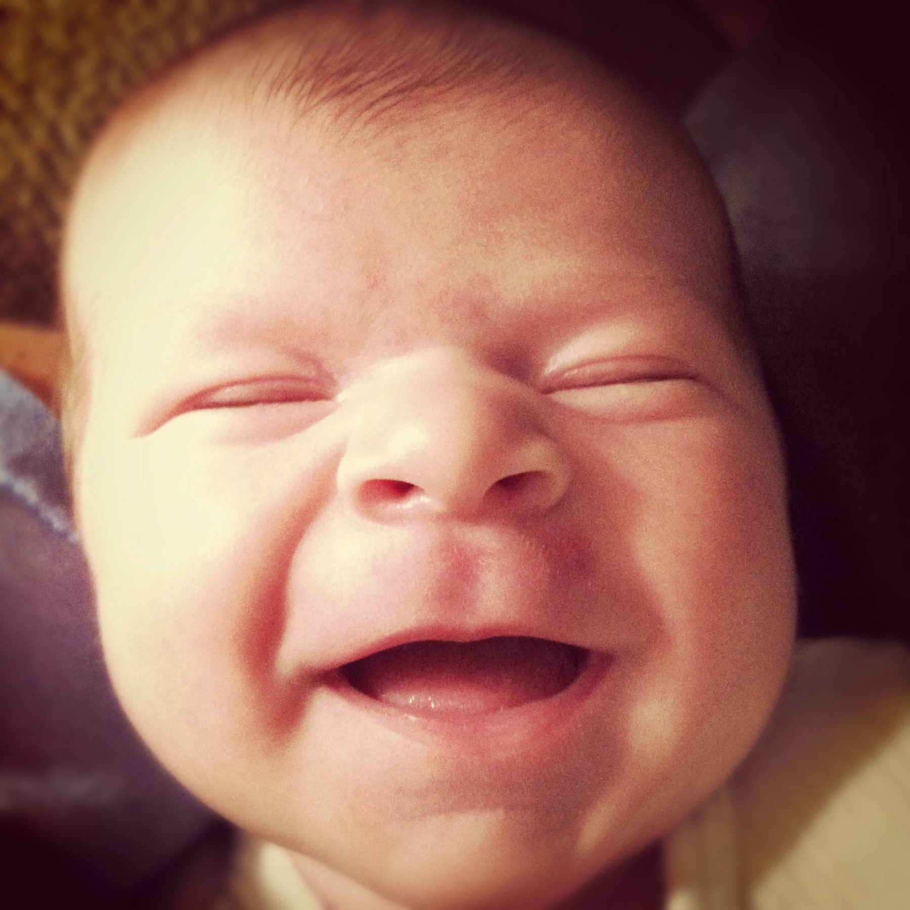 A newborn baby is smiling contentedly with eyes closed.